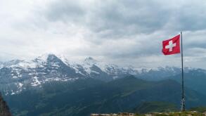 Swiss flag flown in strong wind. Bad weather, dark clouds, rain. In the background Eiger, Monch, and Jungfrau mountains.
