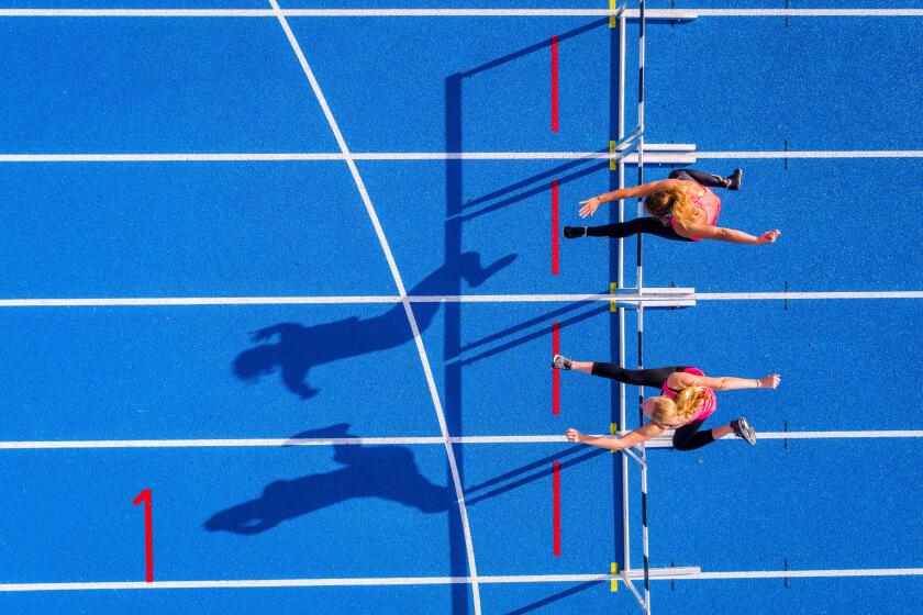Top view of two female runners crossing hurdles on tartan track