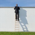 Businessman on ladder looking over wall