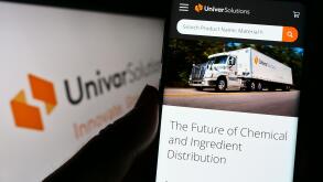 Person holding cellphone with website of US distribution company Univar Solutions Inc. on screen with logo. Focus on center of phone display.