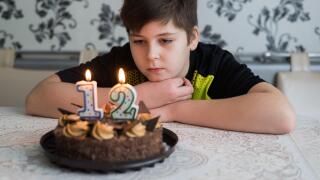 Teen boy looks thoughtfully at cake with candles on twelfth day of birth