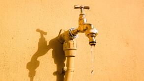 A wall tap on a wall in the sun from which fresh water drips.