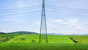 High voltage power line tower standing in a lush green field in Tuscany. Modern infrastructure in a rural spring landscape near Volterra, Italy