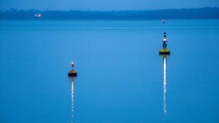 Two buoys marking the navigation channel.  Lights reflected on the water on a calm evening in winter.  The sea is pale blue.