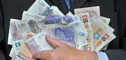 Business man in suit and tie with hand holding a stack of sterling bank notes concept image for cash in hand greed rewards bonus businessman expenses