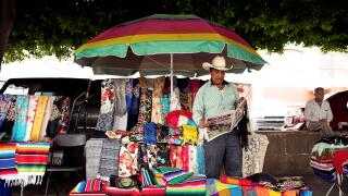 Mexican vendor reading newspaper at his market stall selling colourful textiles at Mercado Hidalgo. Guanajuato, Mexico. Jun 2019