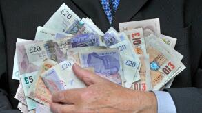 Business man in suit and tie with hand holding a stack of sterling bank notes concept image for cash in hand greed rewards bonus businessman expenses