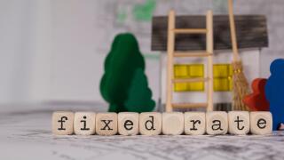 Words FIXED RATE composed of wooden letters. composed of wooden letter. Small paper house, wooden trees in the background. Closeup