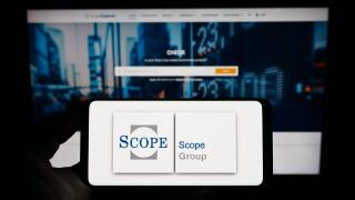 Person holding smartphone with logo of European fund rating company Scope Group on screen in front of website. Focus on phone display.