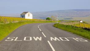 White slow painted sign on B6277 road, barn in flower meadow. Forest in Teesdale, North Pennines, Durham Dales, County Durham.