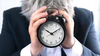Businessman covering face with clock. Time management or seadline concept.