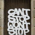 Graffiti with the message 'Can't Stop Won't Stop' on a wire mesh window grille in a historic stone doorway in Barcelona, Spain.