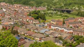 Elevated view of a British suburban neighborhood with rows of houses nestled among lush greenery under a bright blue summer sky