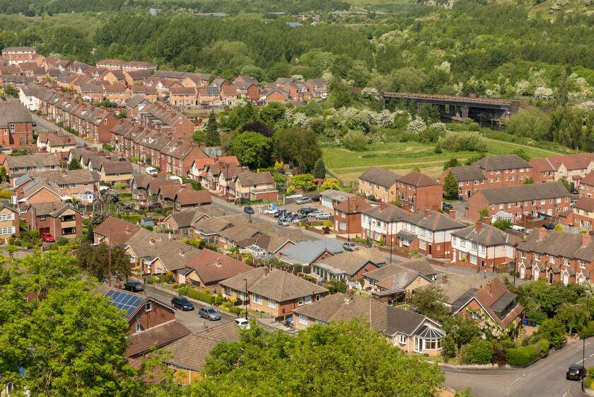 Elevated view of a British suburban neighborhood with rows of houses nestled among lush greenery under a bright blue summer sky
