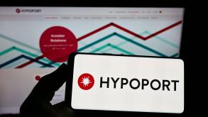 Person holding smartphone with logo of German technology company Hypoport SE on screen in front of website. Focus on phone display.