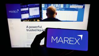 Person holding mobile phone with logo of British financial services company Marex Group on screen in front of web page. Focus on phone display.