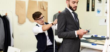 Portrait of handsome young man being fitted in bespoke suit by tailor in traditional atelier studio