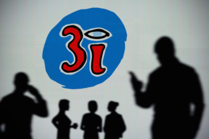 The 3i Group logo is seen on an LED screen in the background while a silhouetted person uses a smartphone (Editorial use only)