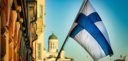 National flag of Finland in central Helsinki with Helsinki Cathedral and blue sky on the background. November 2021.