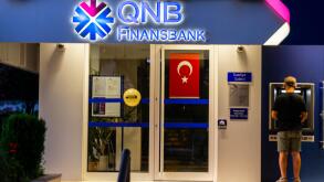 Turkish banks - QNB Finansbank  - colorful bank buildings illuminated.  Kadikoy Istanbul Turkey. Young man withdrawing money in ATM