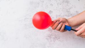 Close up hand blowing red balloon with pump against wall