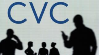 The CVC Capital Partners logo is seen on an LED screen in the background while a silhouetted person uses a smartphone (Editorial use only)