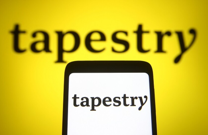 In this photo illustration a Tapestry, Inc. logo of an US multinational luxury fashion holding company is seen on a smartphone and a pc screen.