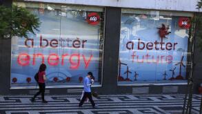 Two people walking past signs in the store window of EDP power company depicting a better energy a better future, Lisbon Portugal
