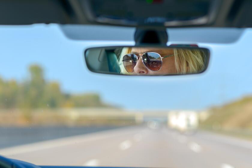 Woman driving a car on a motorway with a view ahead through the windscreen and her glasses reflected in the rear view mirror