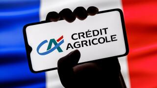Smartphone with Credit Agricole bank logo in clenched hand on background of France flag