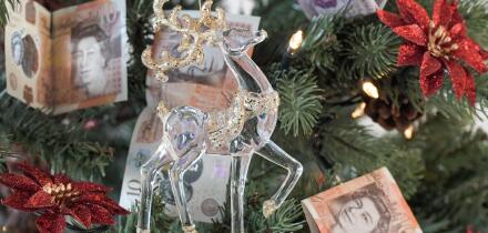 Christmas Tree with ten pound and twenty pound notes as decoration with a glass and gold reindeer in the foreground, expensive Christmas