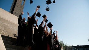 A group of Aberystwyth university students graduating on graduation day, throwing their caps in the air, UK