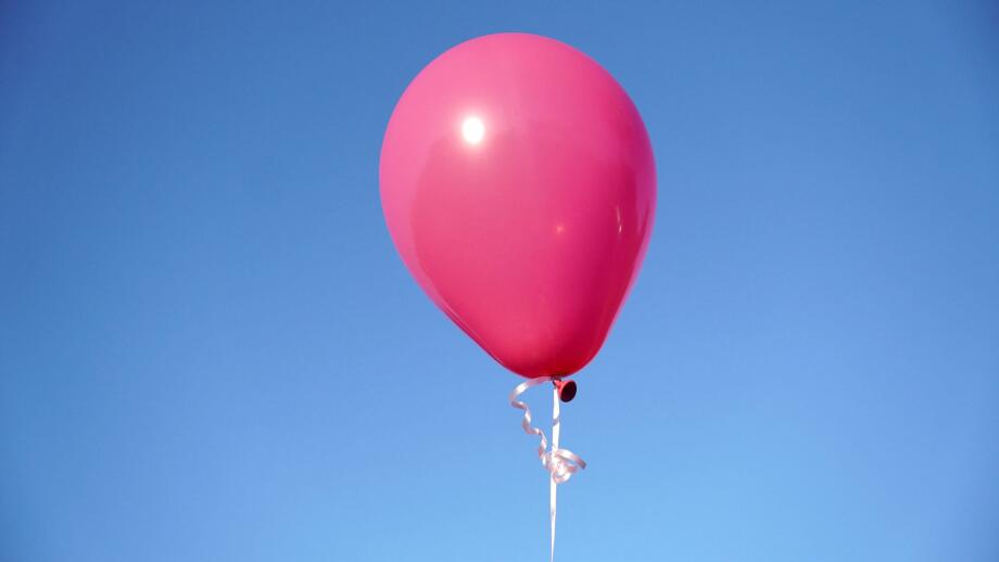 A single pink balloon against the blue sky in closeup