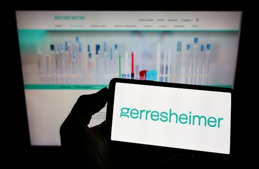 Person holding smartphone with logo of German packaging company Gerresheimer AG on screen in front of website. Focus on phone display.
