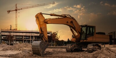 A large excavator at a construction site with cranes and scaffolding in the background