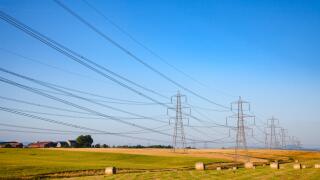 Summer rural landscape with wrapped hay bales on a field and high-voltage power lines in Scotland UK