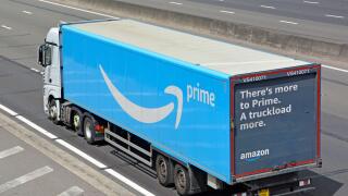 Aerial side & back view of white lorry truck blue Amazon supply chain articulated delivery trailer with advertising on rear door travel on UK motorway