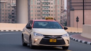 Close-up of Dubai Taxi as it passes a curve on the road in the urban city of Dubai, United Arab Emirates. Shot in the day. Buildings in the background.