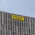 The top corner of the modern Stedin office building, showing its distinctive facade and the company's bright yellow logo against a grey sky. Rotterdam