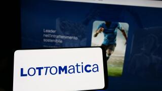 Person holding cellphone with logo of Italian gambling company Lottomatica SpA on screen in front of business webpage. Focus on phone display.